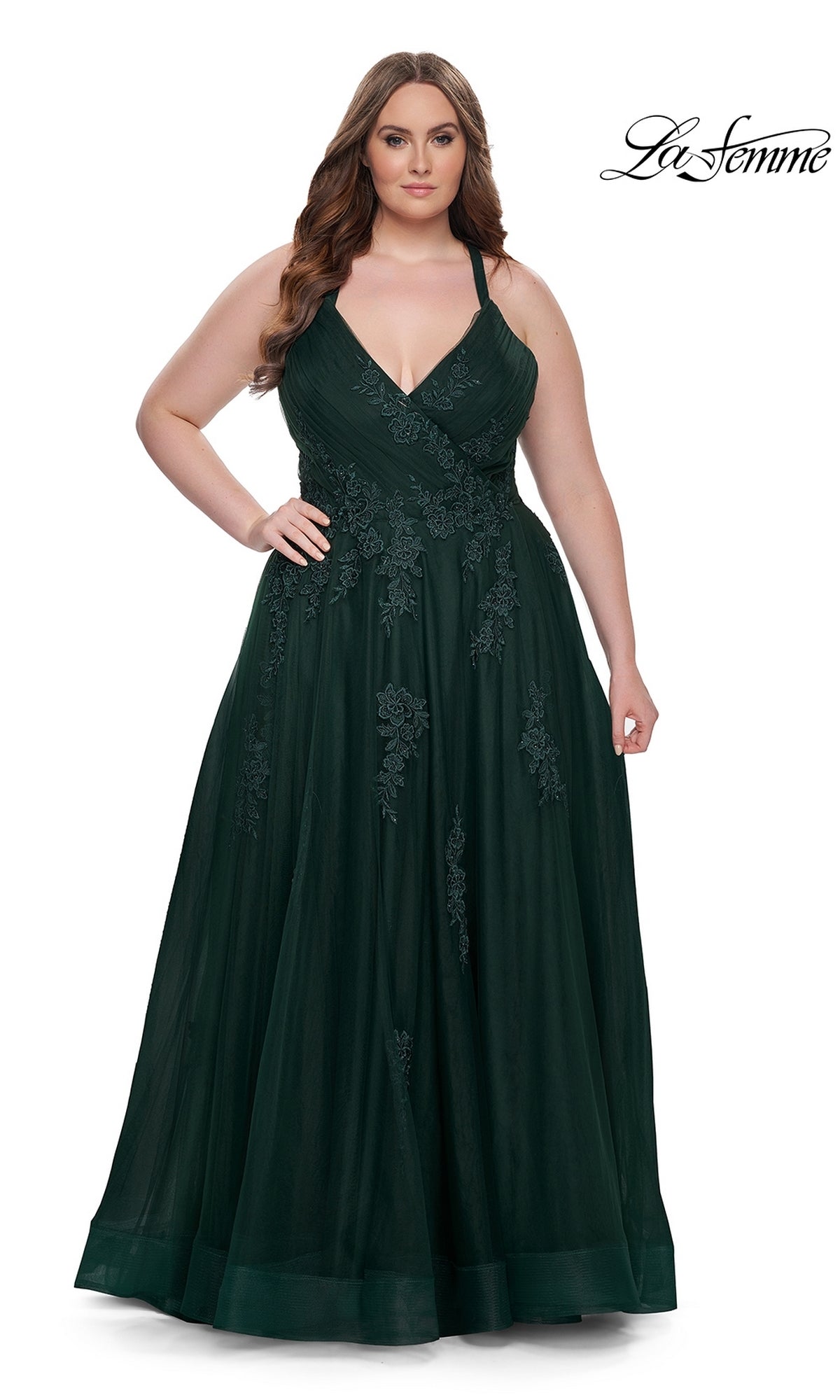 A woman models the La Femme Long Prom Dress 29021—a dark green, floor-length, sleeveless gown with floral lace embroidery—posing with one hand on her hip against a white background.